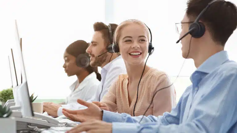 vier Personen mit Headset auf einem Bild, zwei schauen auf den PC, die zewi Personen im Vordergrund unterhalten sich