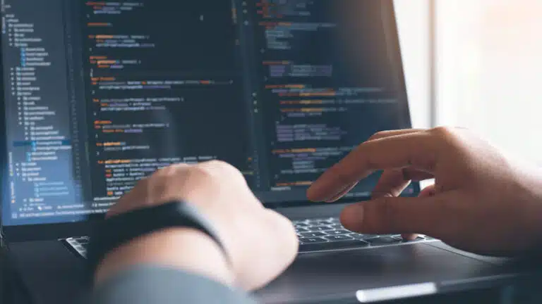 Laptop mit Entwicklercode, zwei Hände die auf der Tastatur sind