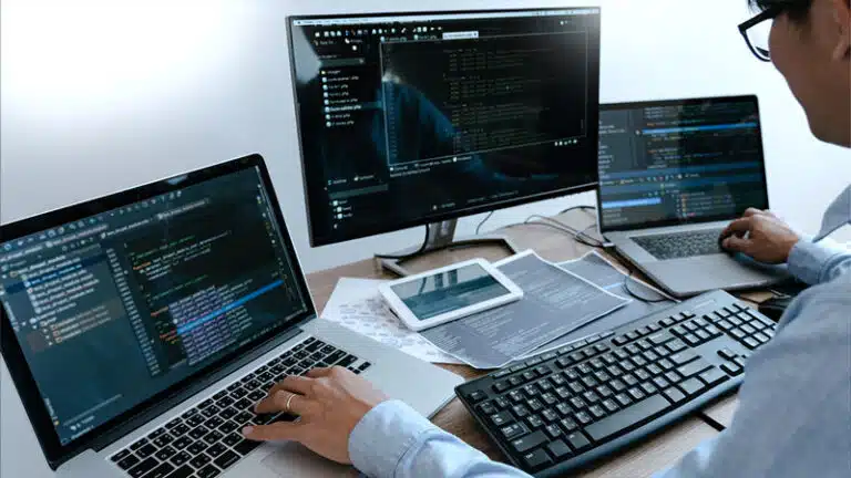Ein Mann arbeitet an drei Bildschirmen mit Entwicklercode
