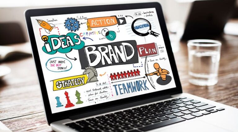 Laptop steht auf einem Tisch, auf dem Laptophintergrund steht in bunter Schrift Wörter wie Brand